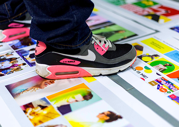 a person wearing Nike Air Max sneakers standing on printed colorful images with various designs and graphics featuring the number 19 in different contexts